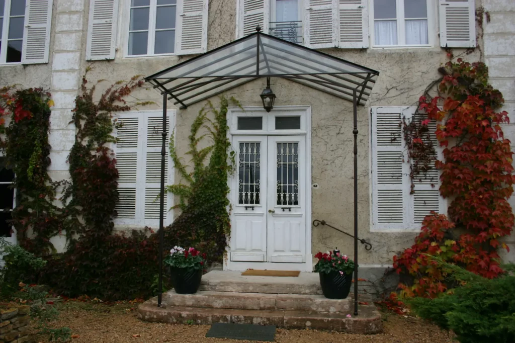 Marquise pyramidale en fer forgé noir et verre sur grand perron de demeure bourgeoise, montants à volutes et épis de faîtage forgé, réalisée sur mesure par Christophe Barbarin ferronnier d'art