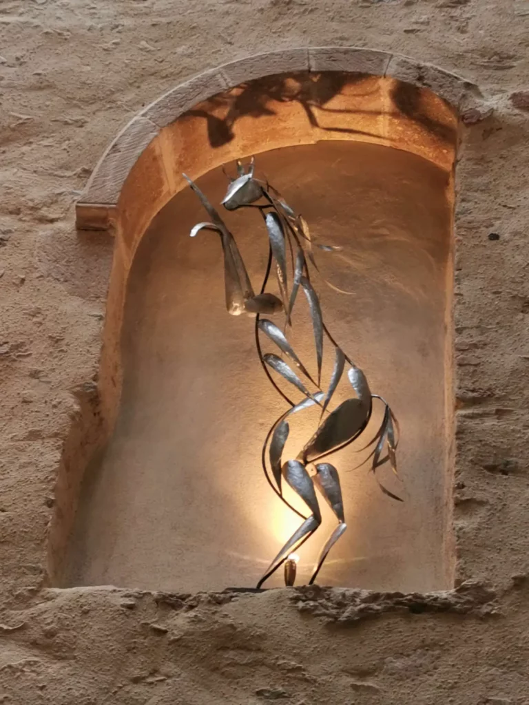 Sculpture d'un cheval cabré en métal inox dans une niche en pierre éclairé par dessous