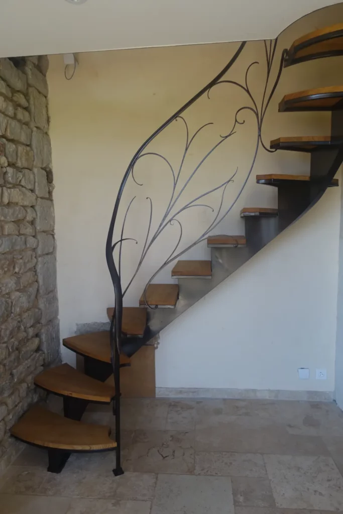 Escalier tournant petit espace sur mesure bois et metal, rampe à volutes forgées.