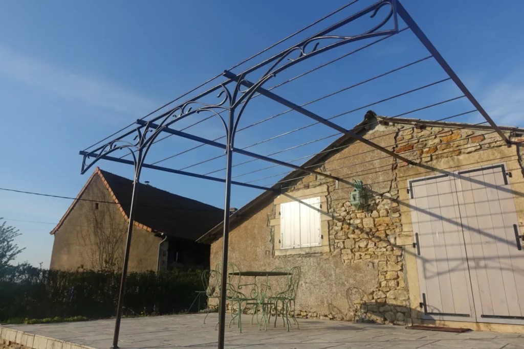 Pergola en fer forgé noir à volutes forgées sur terrasse dallée de propriété en pierre, structure aérienne sur mesure, réalisée par Christophe Barbarin ferronnier d'art Lyon Bourgogne